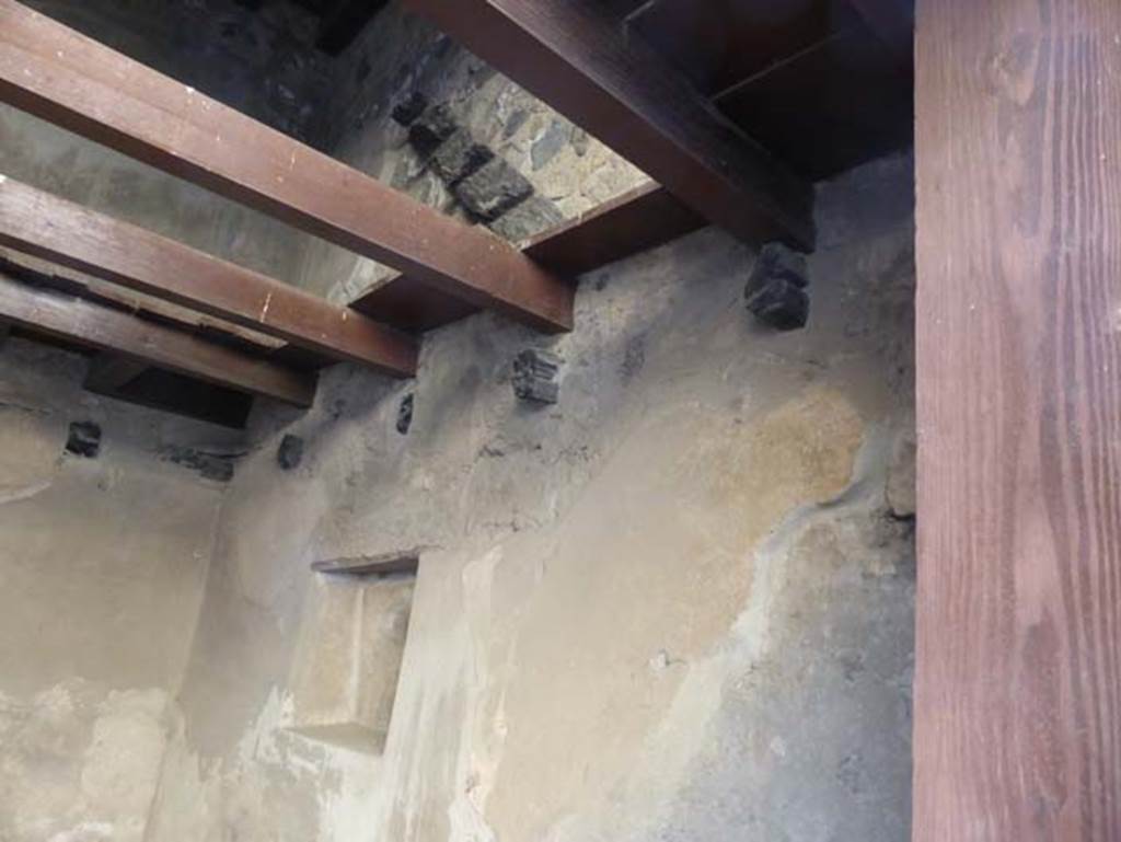 VI 15 Herculaneum, September 2015. West wall with square niche, remains of carbonised floor/ceiling support beams, and stairs/ladder to an upper floor.
As described by Camardo and Notomista, the reconstructed beams for the ceiling are set higher in the wall, because of the carbonised remains of the original beams set below.